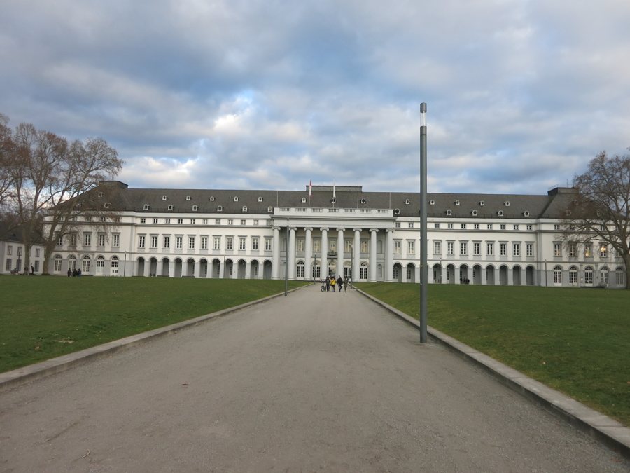 Weißes Schloss mit Säulenportikus am Ende eines Weges durch eine Rasenfläche.