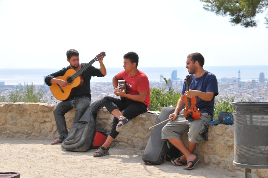 Drei Musiker spielen Gitarre und Geige vor der Skyline von Barcelona